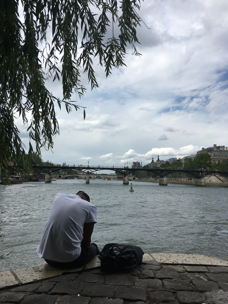 Young man hunched over the Seine at the tip of Square du Vert-Galant looking west (2019)